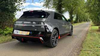 Static rear 3/4 shot of a gray 2025 Hyundai Ioniq 5 N parked on a country road lined with trees.