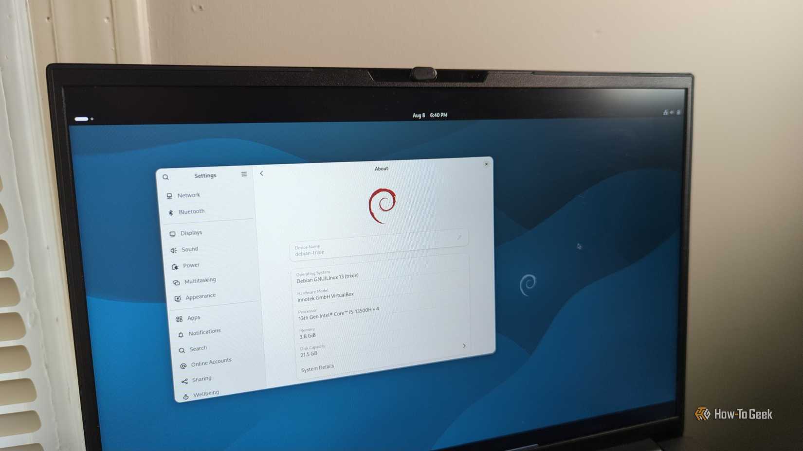 Uma tela de laptop com Debian 13 e a área de trabalho Gnome visíveis.