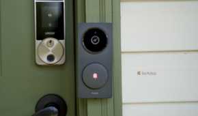 A head-on shot of the Aqara Doorbell Camera Hub G410 mounted to a green door frame with cream house siding next to it.