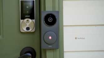 A head-on shot of the Aqara Doorbell Camera Hub G410 mounted to a green door frame with cream house siding next to it.