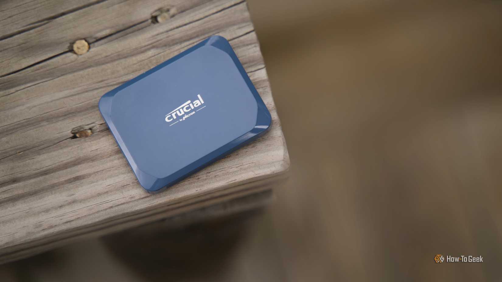 Crucial X10 portable SSD sitting on wooden deck with blurred background.