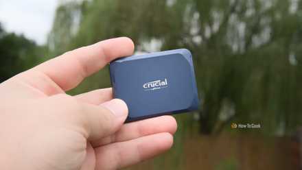 A hand holding the Crucial X10 portable SSD with a weeping willow tree in the background.