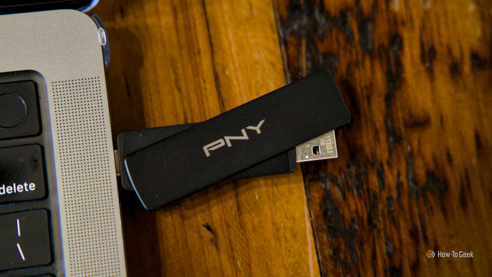 PNY Duo Link V3 ফ্ল্যাশ ড্রাইভটি একটি কাঠের টেবিলে বসে থাকা একটি MacBook Pro-এ প্লাগ করা হয়েছে, যেখানে USB-A পাশ সামান্য আটকে আছে৷