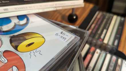 Close-up of the price tag on a CD case reading $5, surrounded by other CD albums.