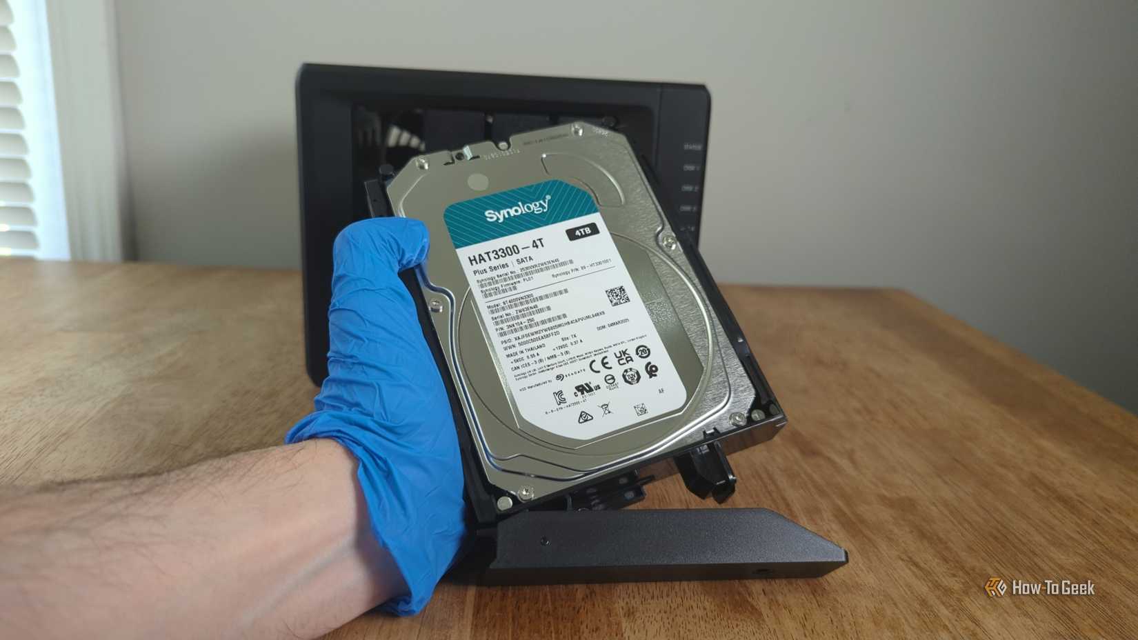 A person's gloved hand holds a Synology hard drive in front of a Synology DS425+ NAS.-2