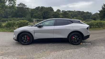Static side profile shot of a gray 2025 Lotus Eletre 600 Sport SE parked on gravel with trees in the background.