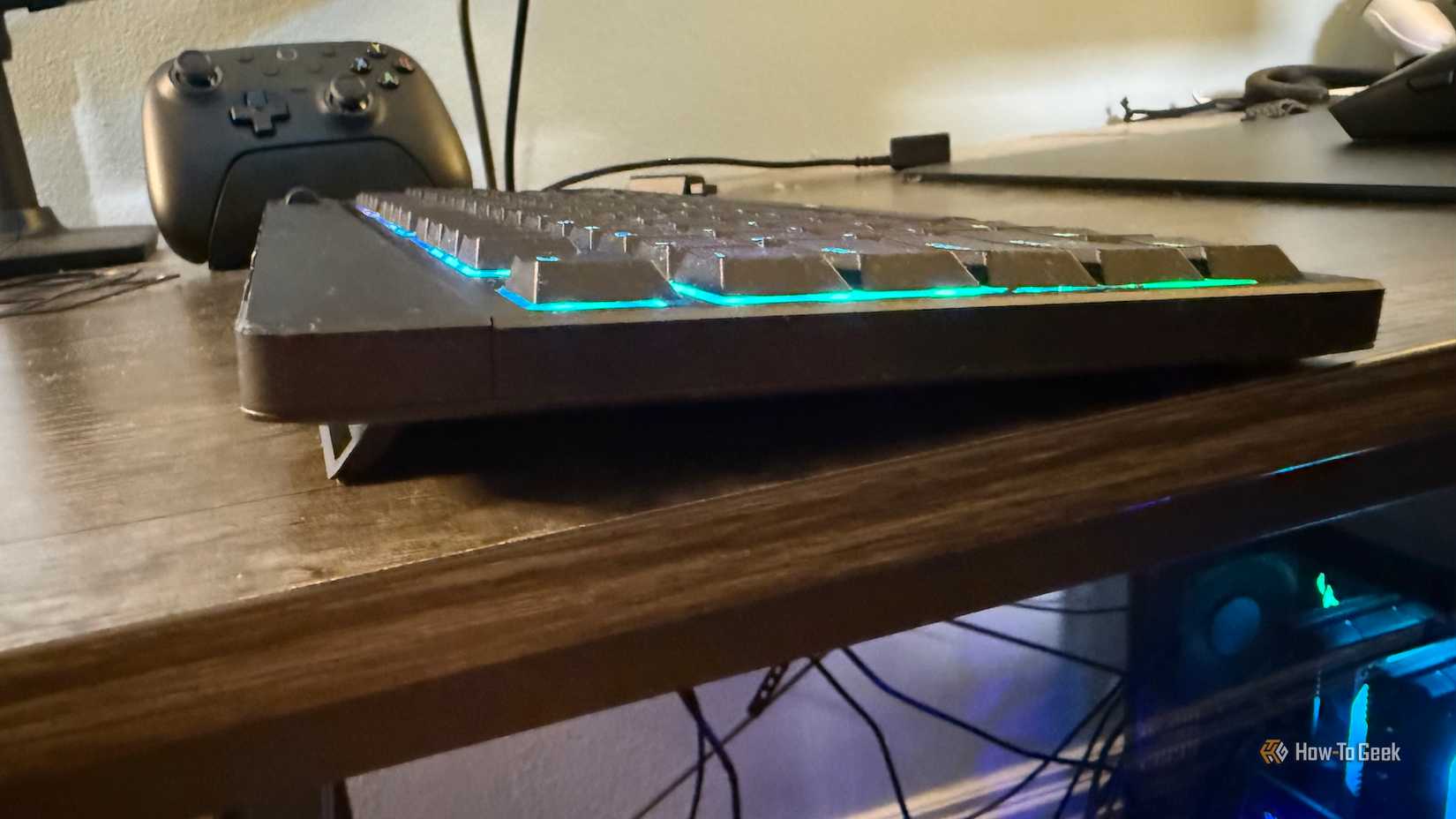 O Razer Blackwidow V4 de baixo perfil Tenkeyless Hyperspeed do lado com um controlador de jogo em segundo plano.