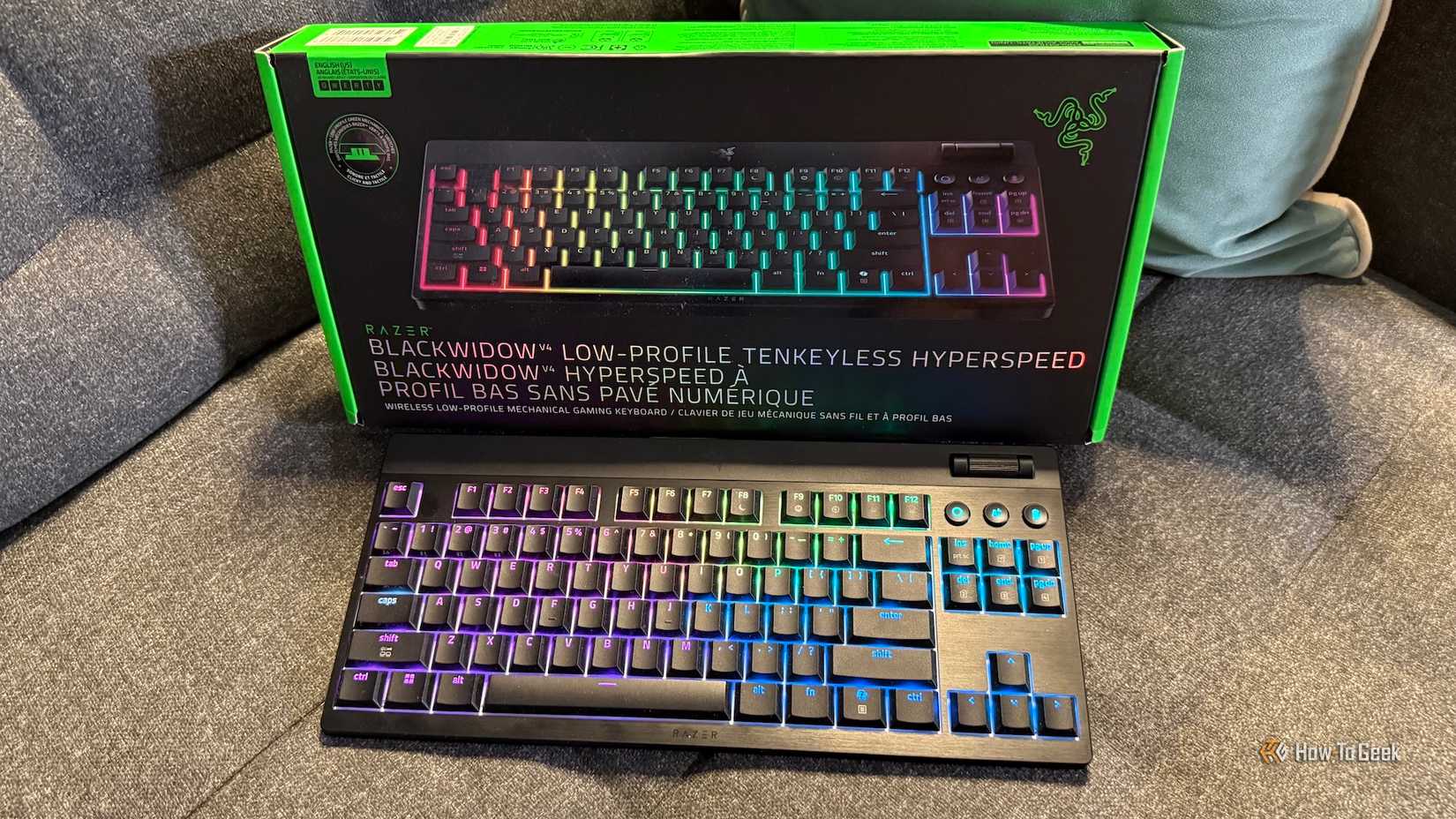 O Razer Blackwidow V4 de baixo perfil Tenkeyless Hyperspeed e sua caixa em um sofá.