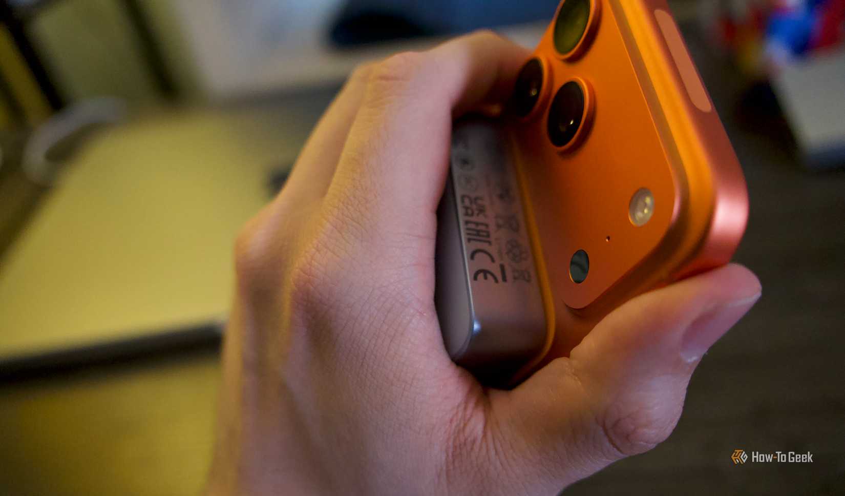 A hand holding an orange iPhone 17 Pro Max with a Ugreen MagFlow 10000mAh 25W Power Bank attached.