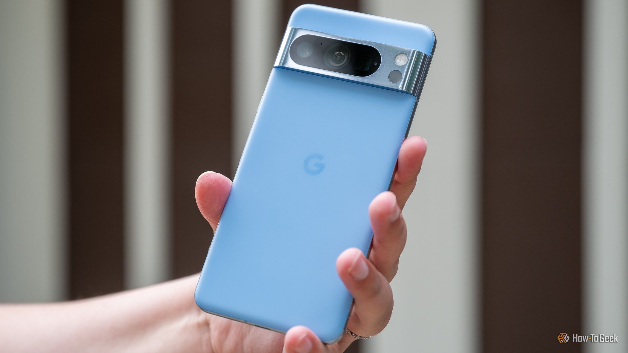 Person holding up the back of a blue Google Pixel 8 Pro phone.