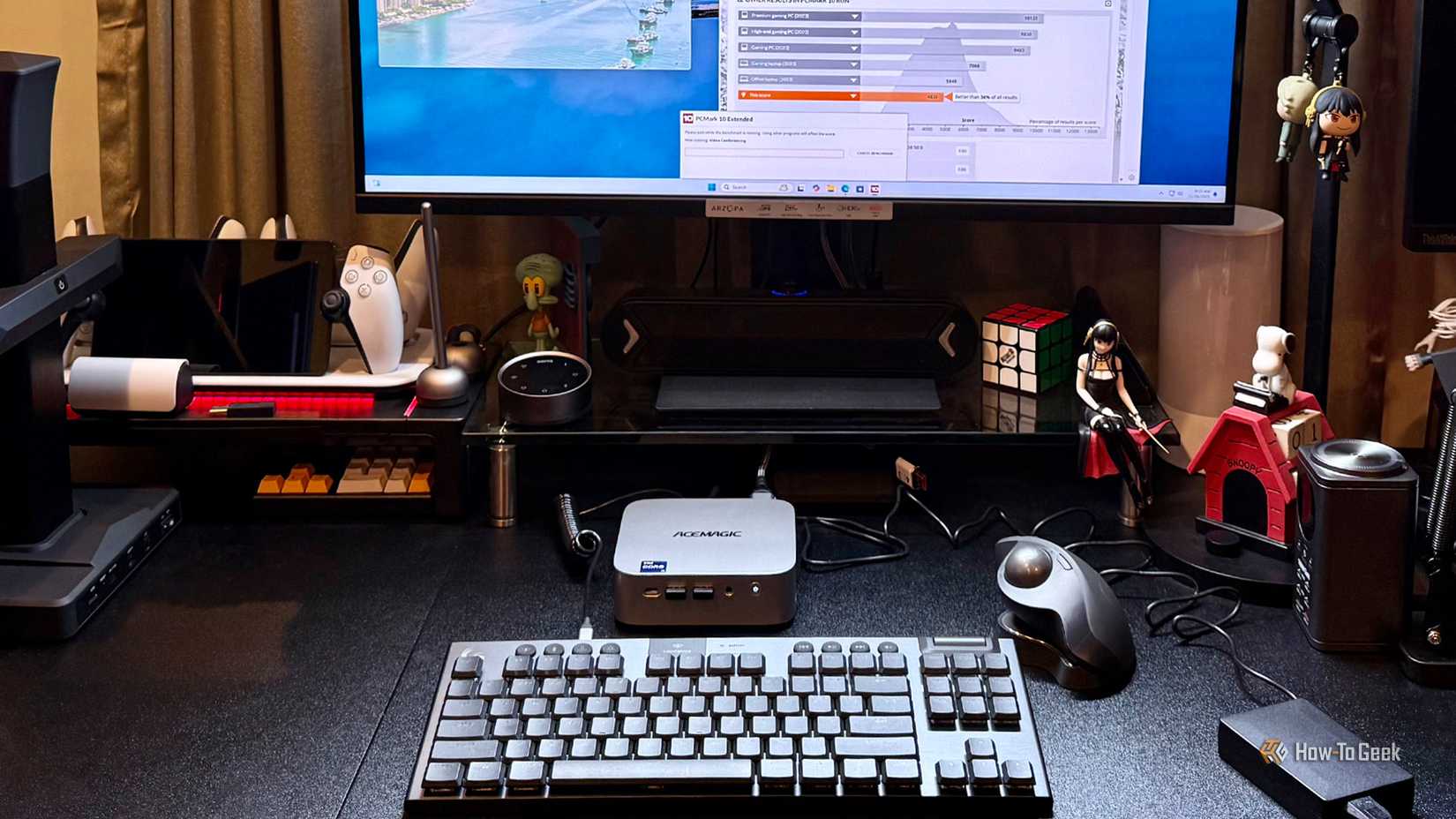 ACEMAGIC M1 Mini PC on a desktop with keyboard, trackball, and monitor running benchmarks.