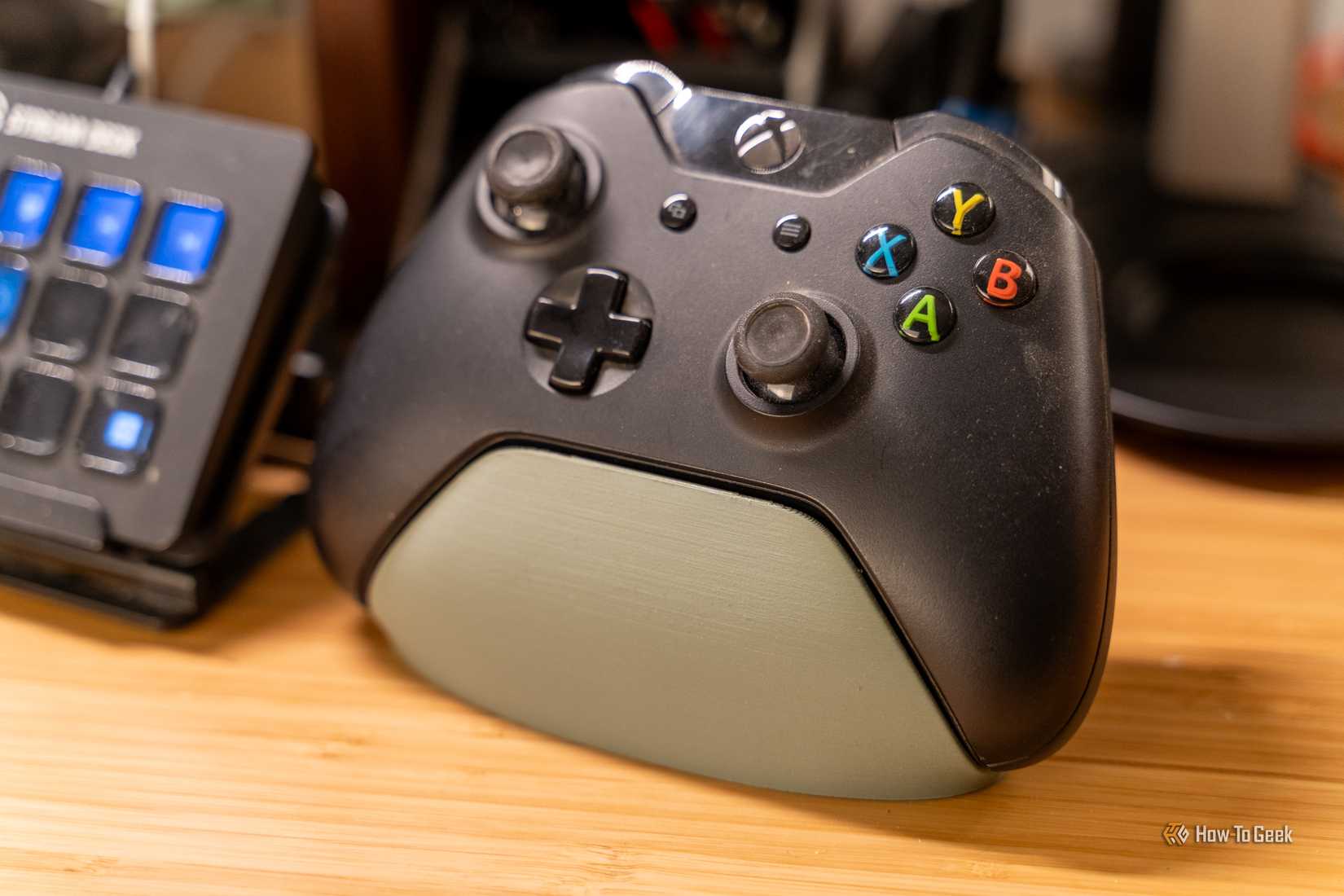 A 3D printed Xbox controller stand holding a controller on a wooden desk.