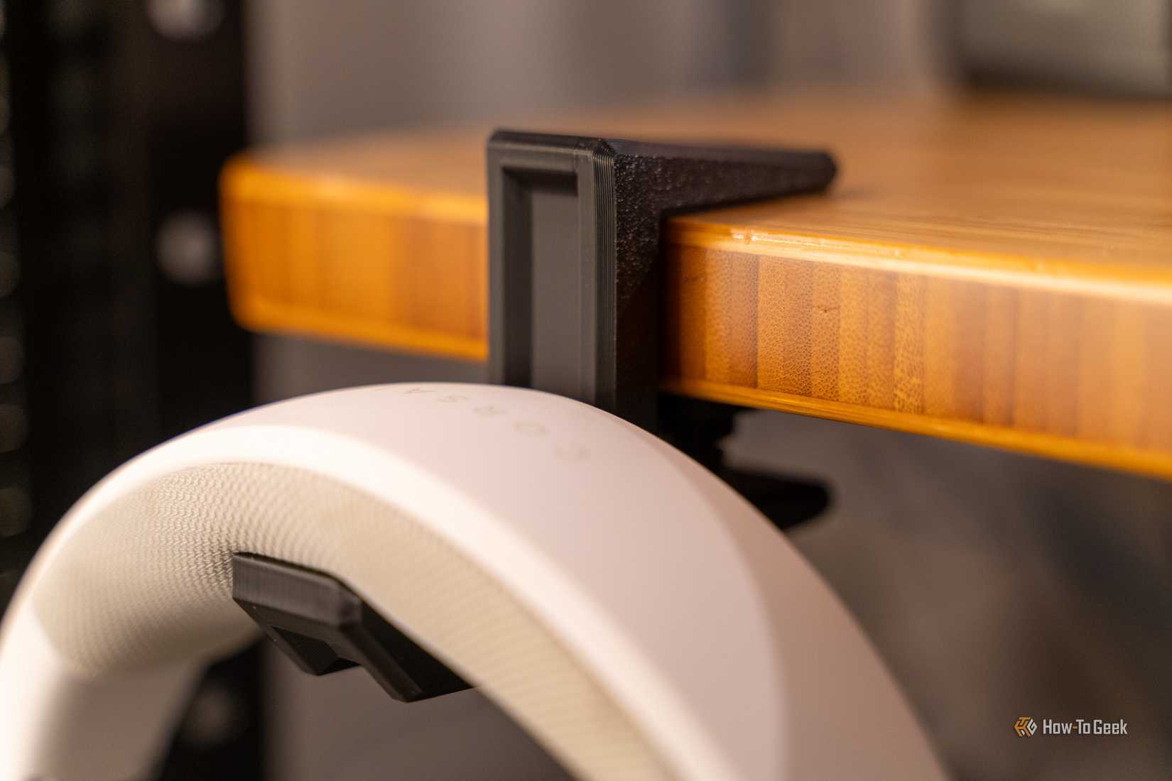 A 3D printed headphone clamp holding a pair of headphones to a desk.