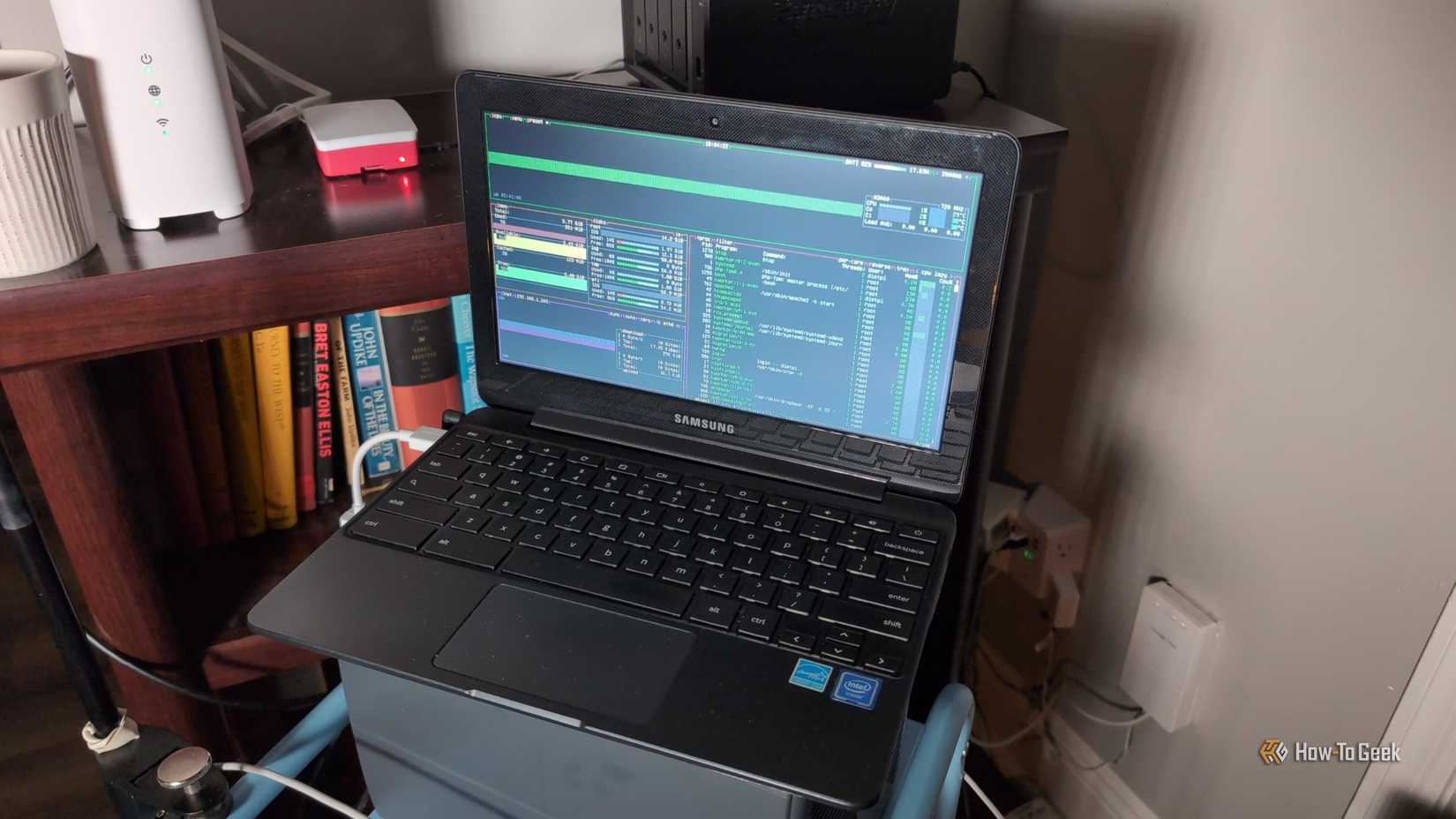 A Chromebook running btop with a router, Raspbery Pi, and NAS in the background.