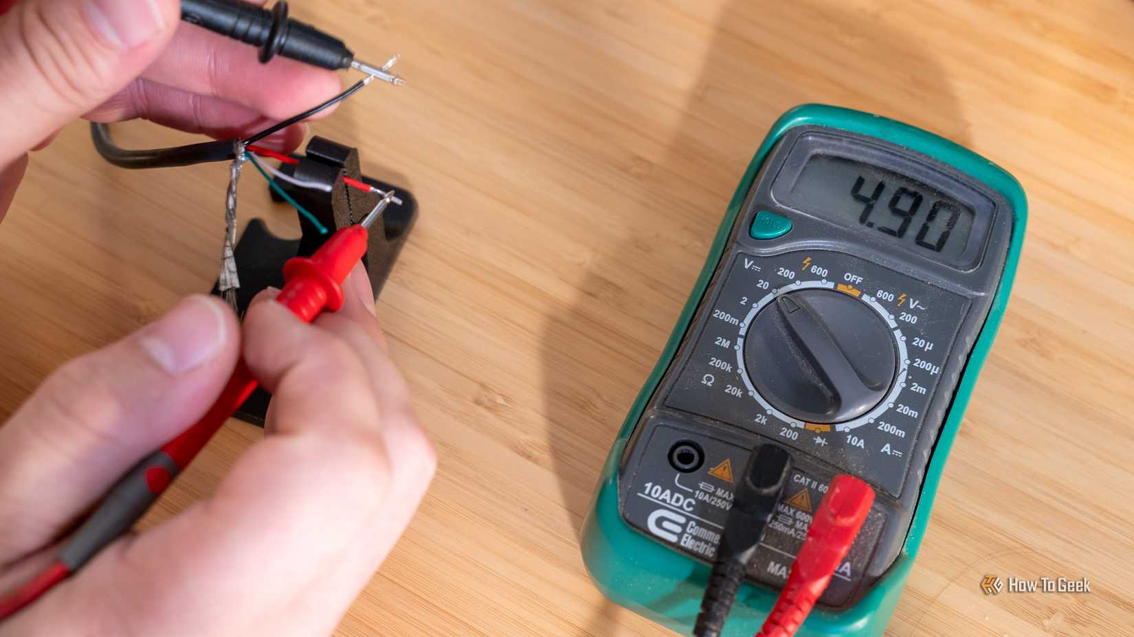 A person using a multimeter to test the positive and negative wires of a USB cable with the multimeter showing 4.9V.