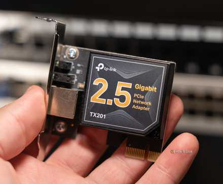A TP-Link 2.5 gigabit PCIe networking adapter held by a person with network switches in the background.