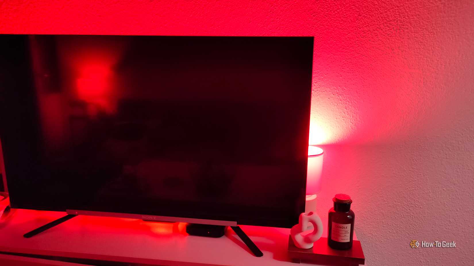 A smart bulb set to red inside a lamp that's behind a TV.