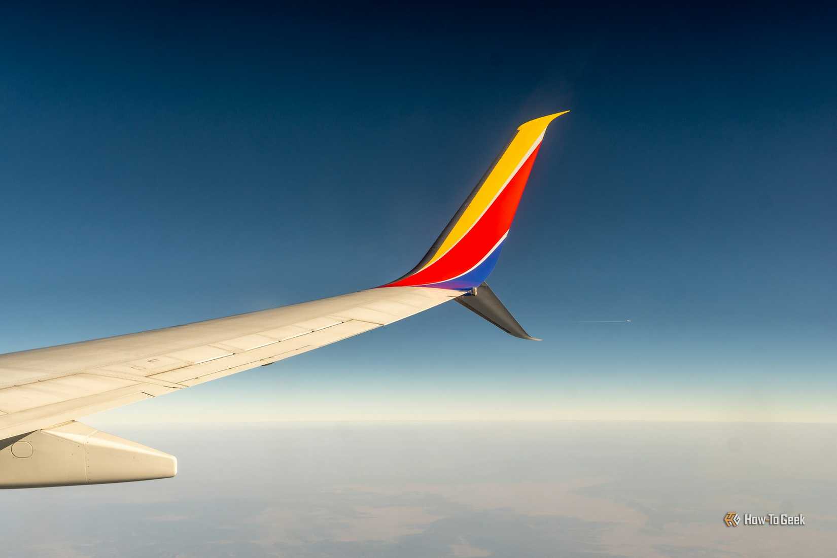 The wing of an airplane in the air with clouds and a dark sky above.