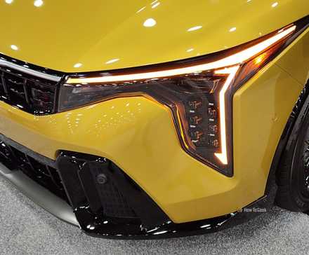 Close-up shot of the headlight and grille on a yellow 2026 Kia K4 Hatchback.