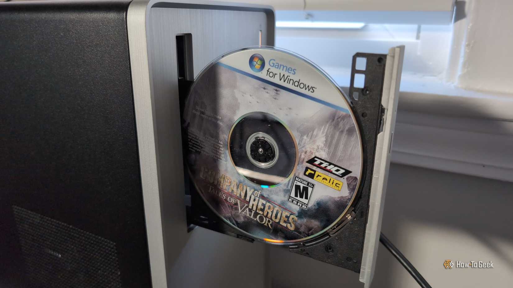 A CD-ROM in an open PC disc drive with a label on the CD reading Games for Windows and the title of the game Company of Heroes Tales of Valor.