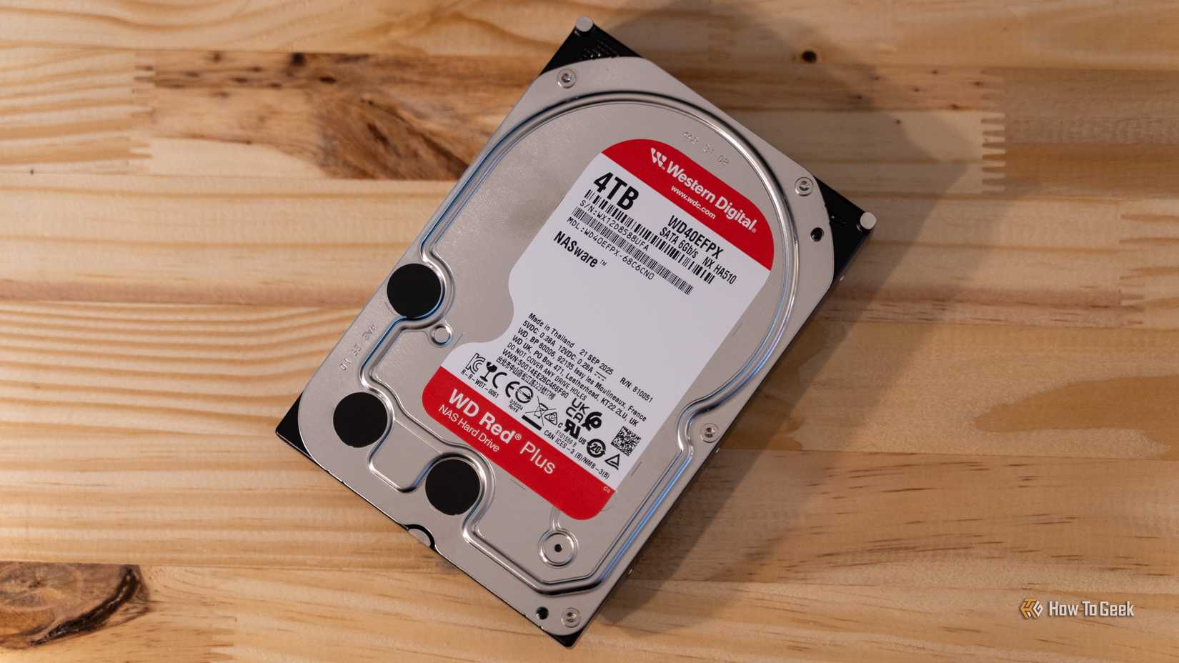 A Western Digital WD Red Plus 4TB NAS HDD sitting flat on a wooden desk.