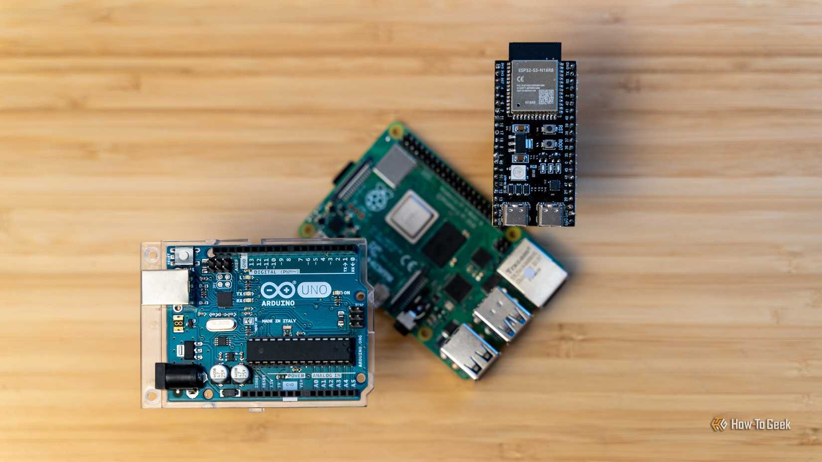 Arduino Uno R3 and ESP32 floating on Raspberry Pi on wooden background.