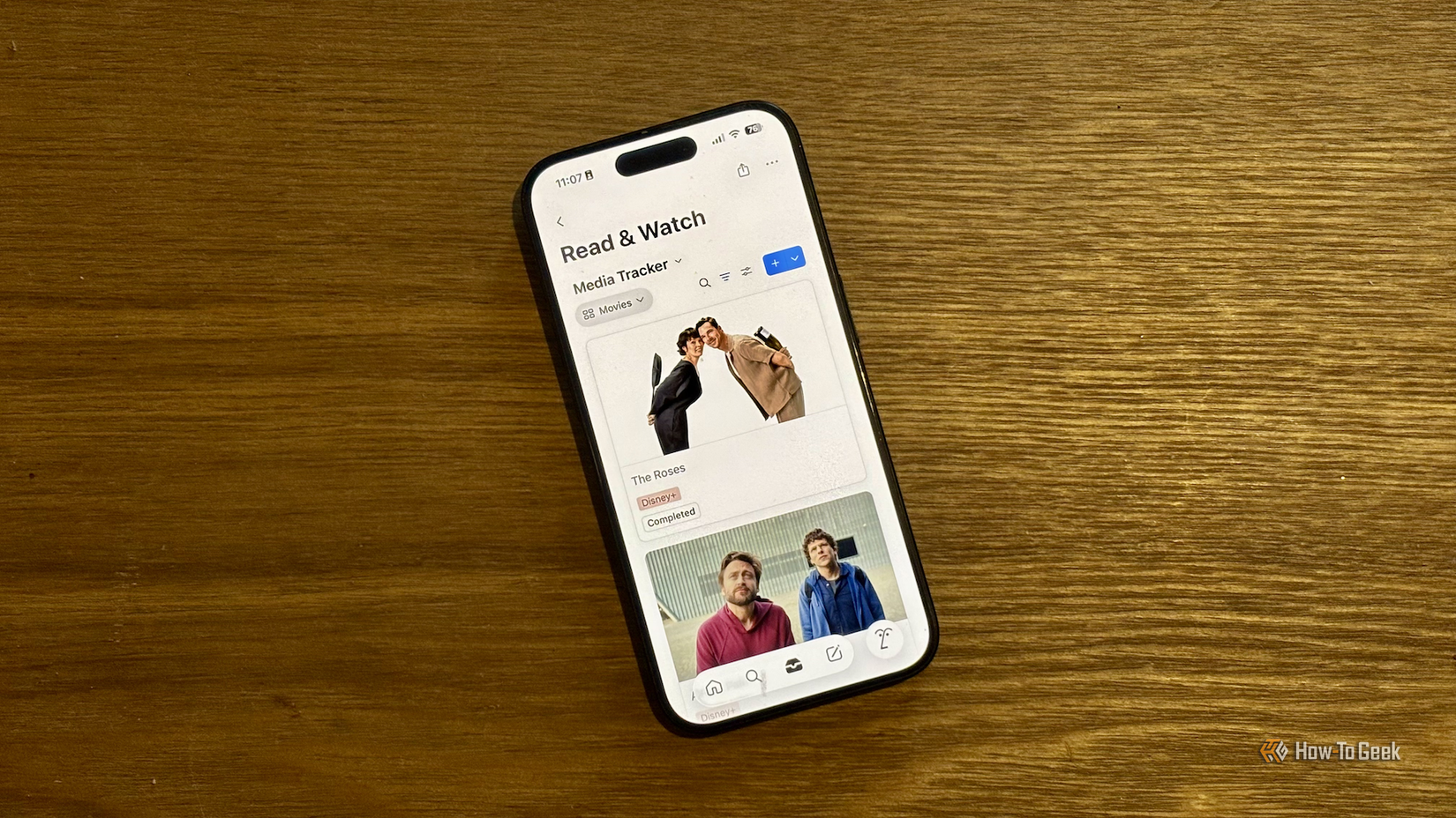An iPhone on a desk showing a media tracker in the Notion app.