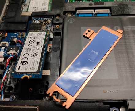 A copper NVMe heatsink with thermal pads next to an NVMe SSD inside of a laptop.