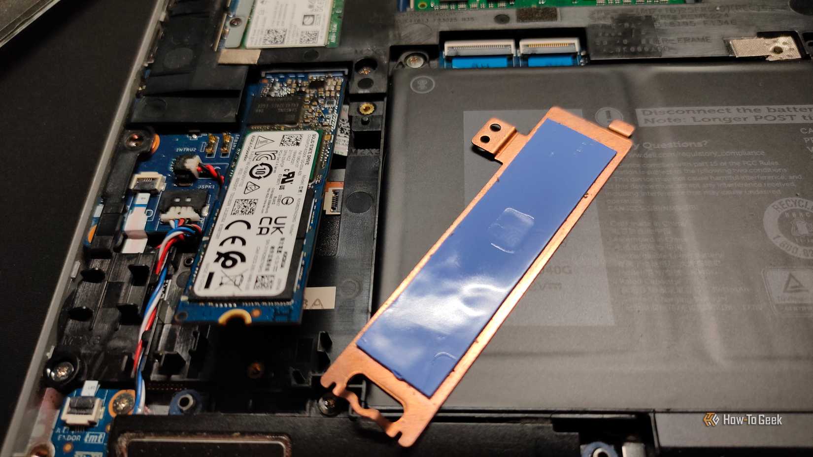 A copper NVMe heatsink with thermal pads next to an NVMe SSD inside of a laptop.