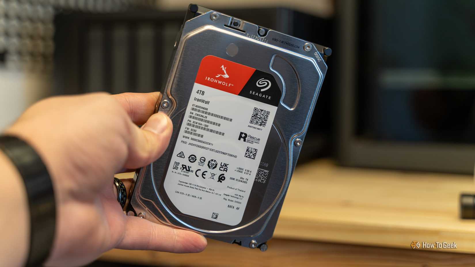 Seagate IronWolf 4TB ハード ドライブを斜めに持ち、ラベルと仕様を示す手。