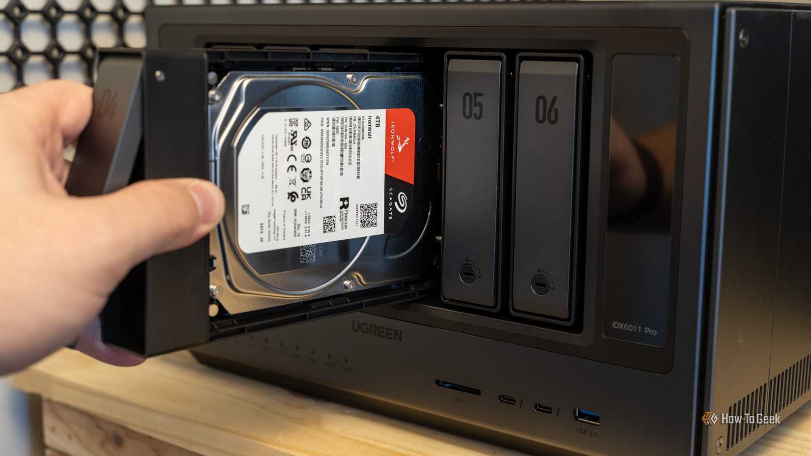 A hand inserting a Seagate IronWolf 4TB hard drive into the Ugreen iDX6011 Pro NAS with the IronWolf label visible.