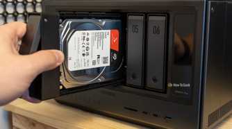 A hand inserting a Seagate IronWolf 4TB hard drive into the Ugreen iDX6011 Pro NAS with the IronWolf label visible.
