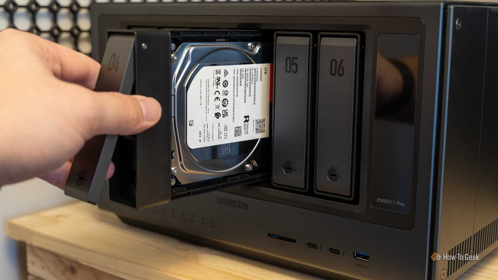 A hand sliding a drive tray with a Seagate IronWolf 4TB hard drive into the Ugreen iDX6011 Pro NAS.