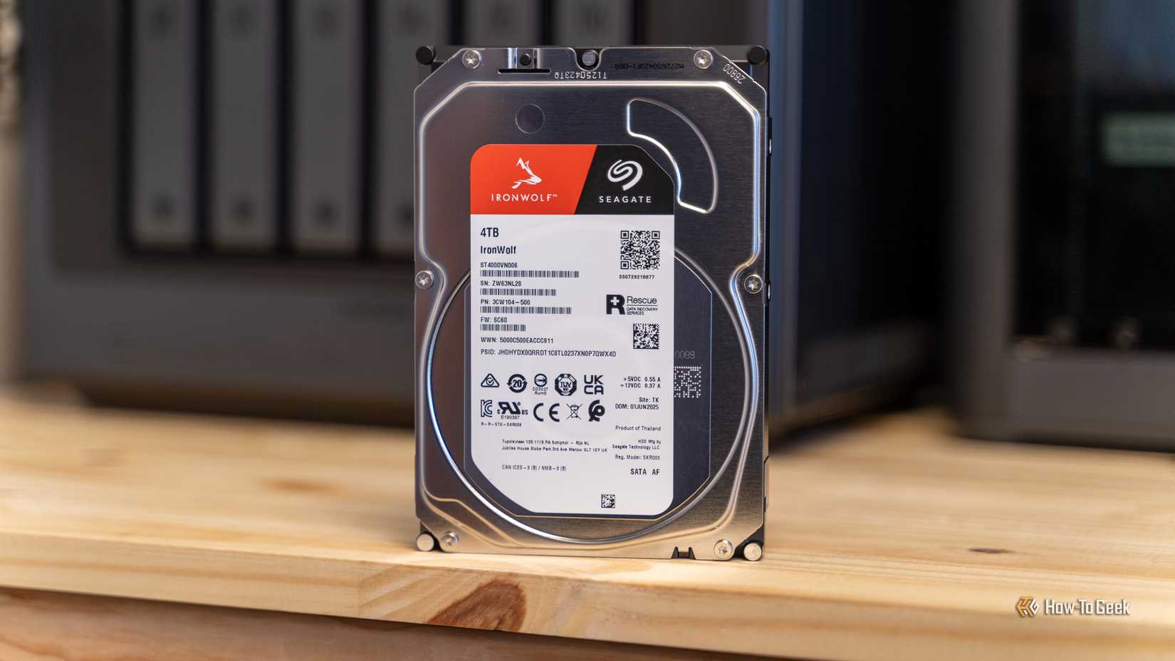 A Seagate IronWolf 4TB hard drive on a desk with the Ugreen iDX6011 Pro NAS slightly out of focus behind it.