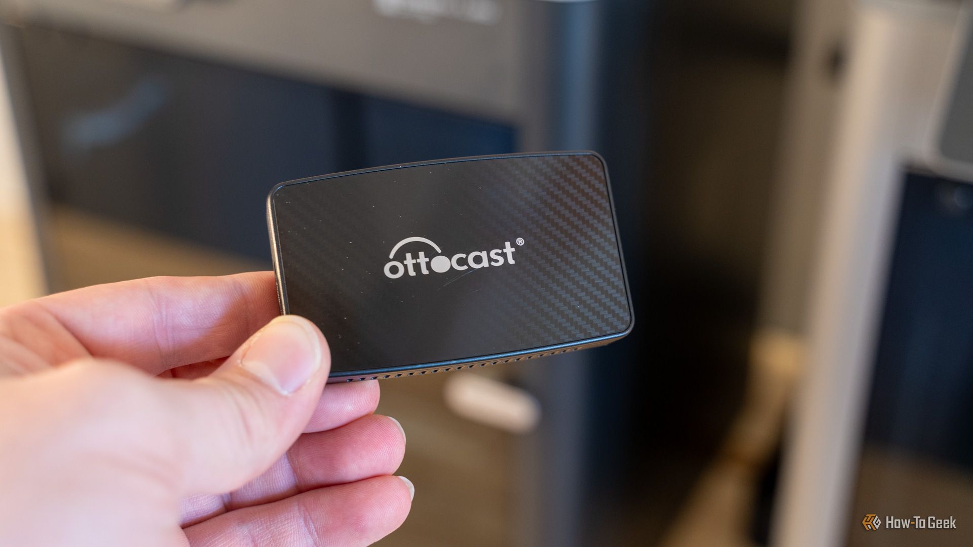 The Ottocast wireless CarPlay adapter held in one hand.