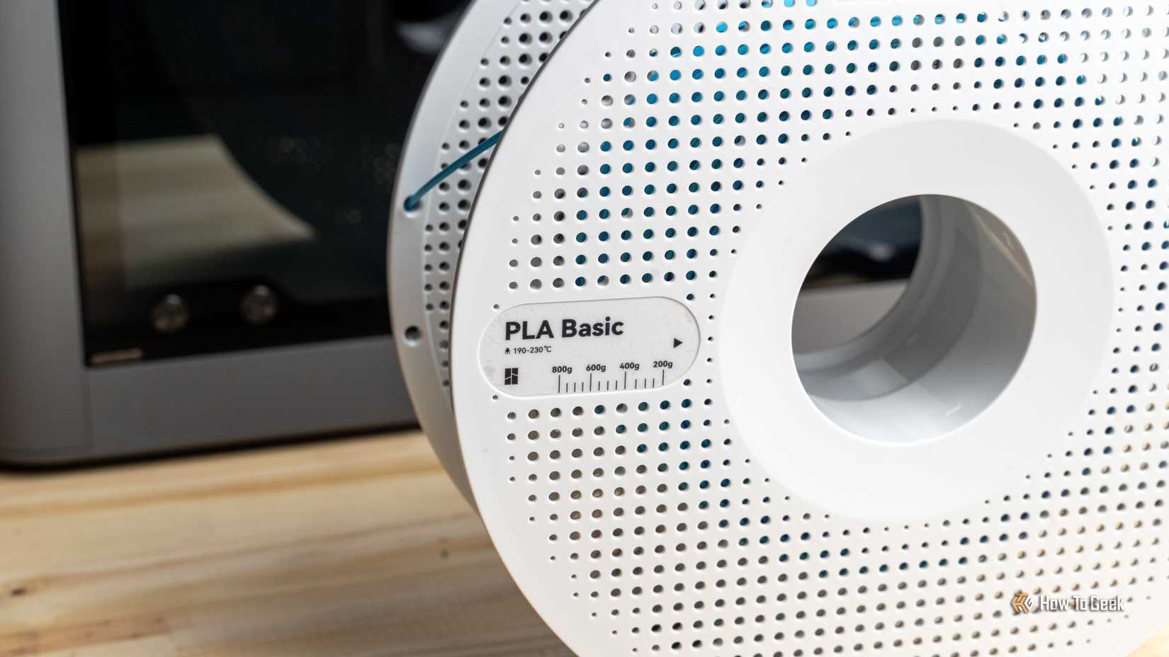 Close-up of a Bambu Lab PLA Basic filament spool label on a wooden desk with a 3D printer in the background.