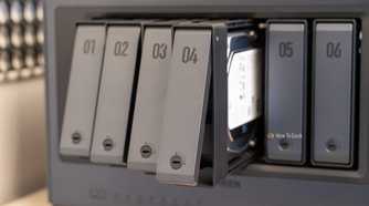 Drive trays fanned out from the Ugreen iDX6011 Pro NAS showing the tool-free tray design and an installed hard drive.