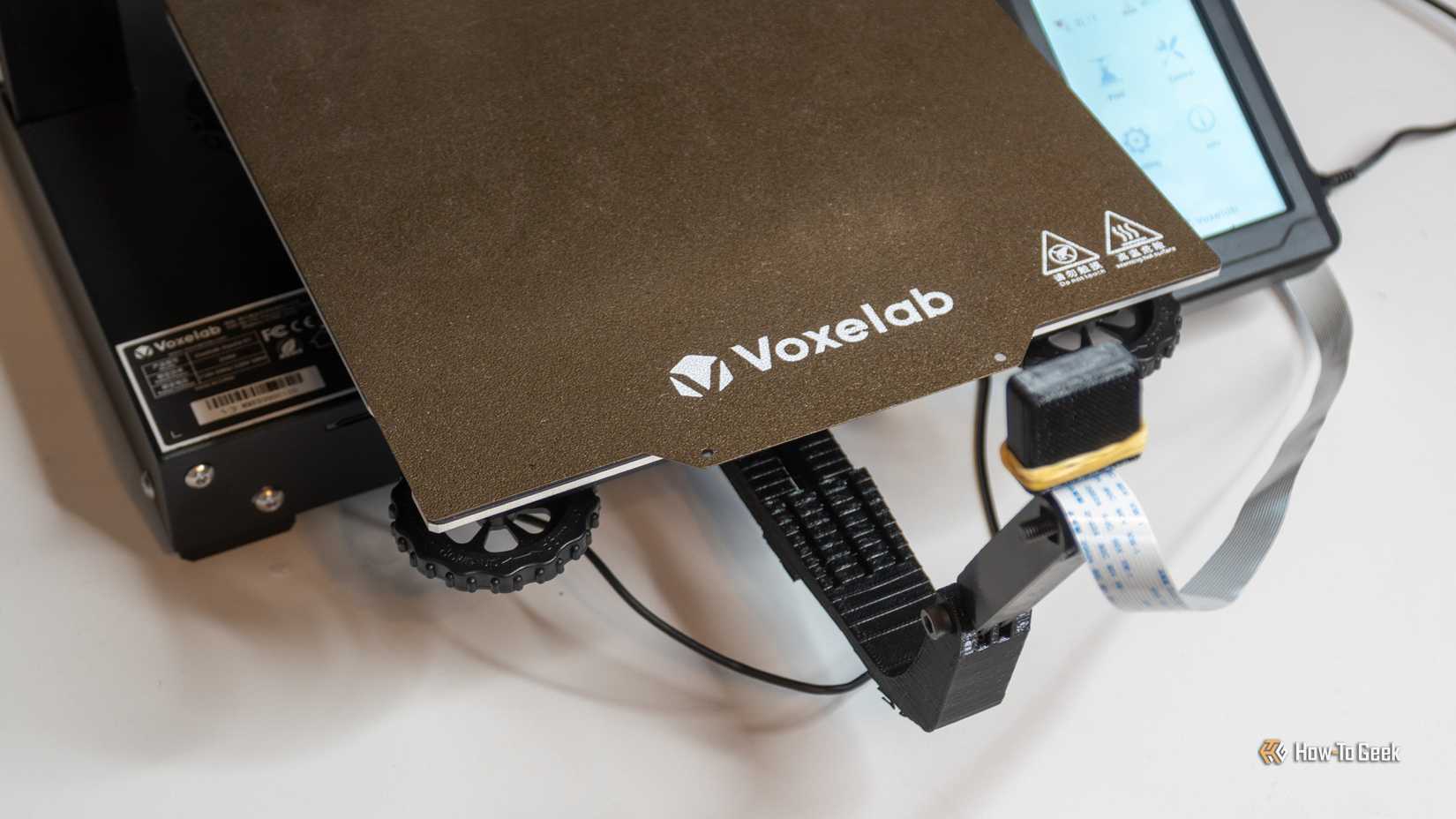 The bed of a Voxelab 3D printer showing the bed leveling knobs.