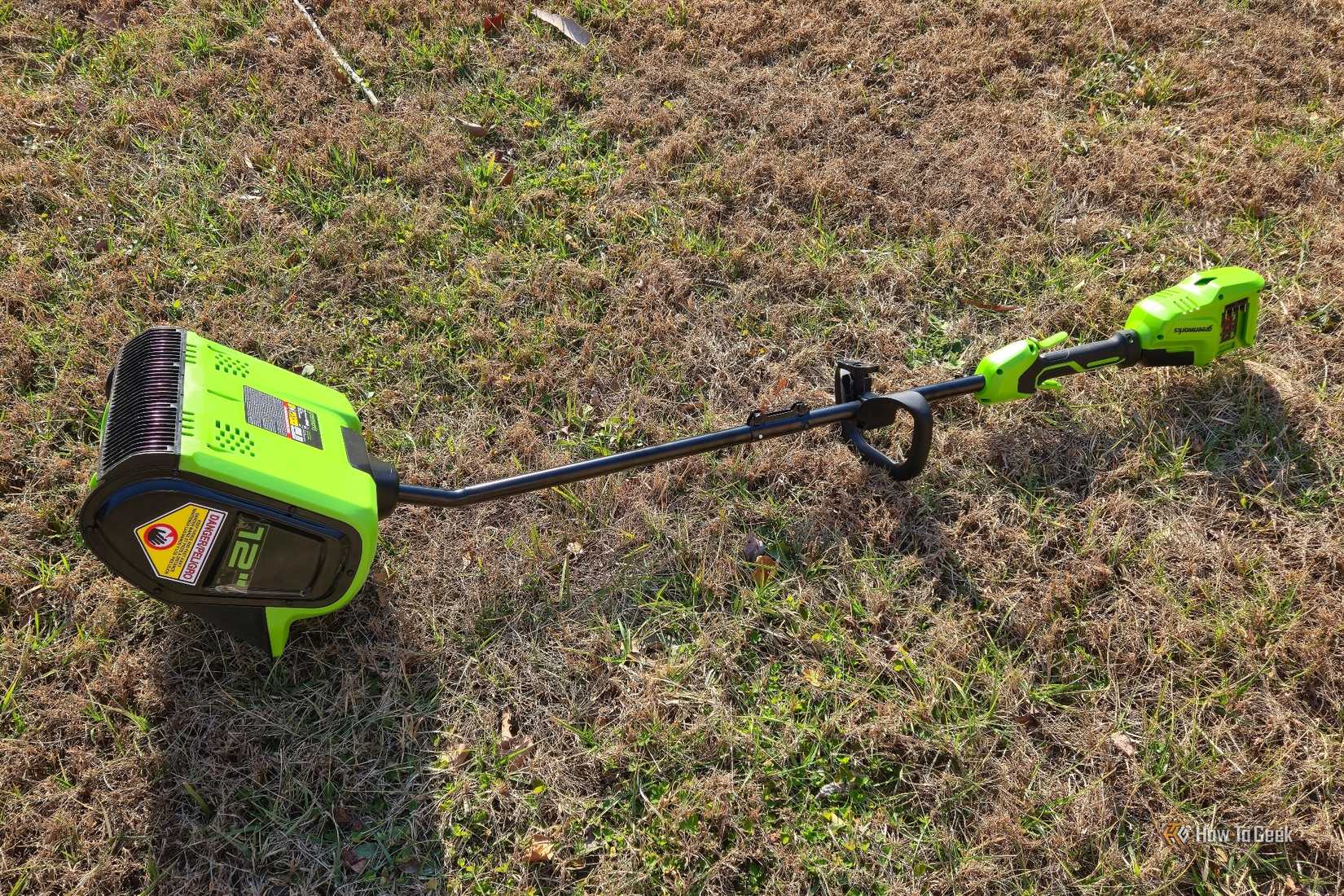 Greenworks 12-inch snow shovel lying in the grass.