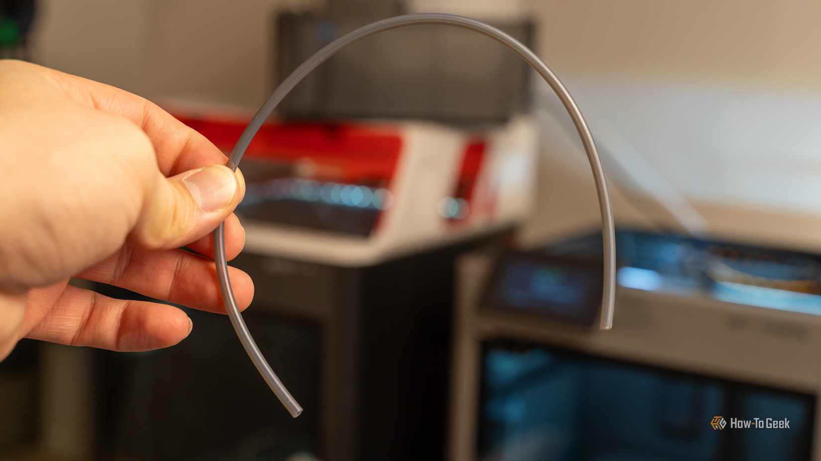 Hand holding a PTFE tube in front of a Bambu Lab printer.