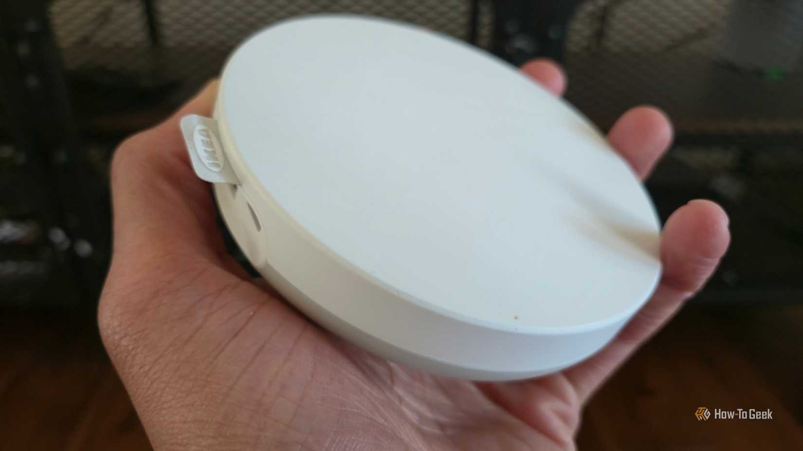 Hand holding an IKEA DIRIGERA smart home hub.