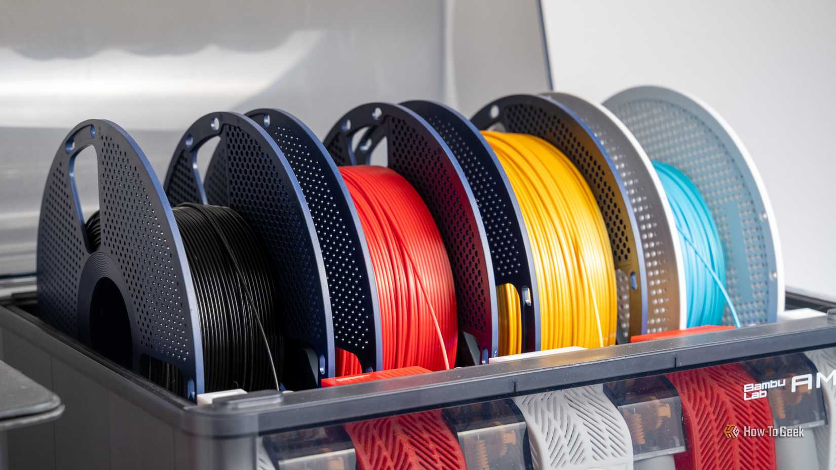 Multiple colorful spools of 3D printer filament loaded inside a Bambu Lab AMS unit.