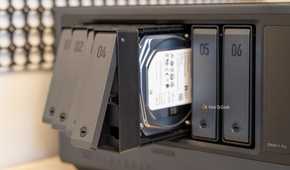 Multiple drive trays pulled out from the Ugreen iDX6011 Pro NAS with a hard drive visible inside the bay.