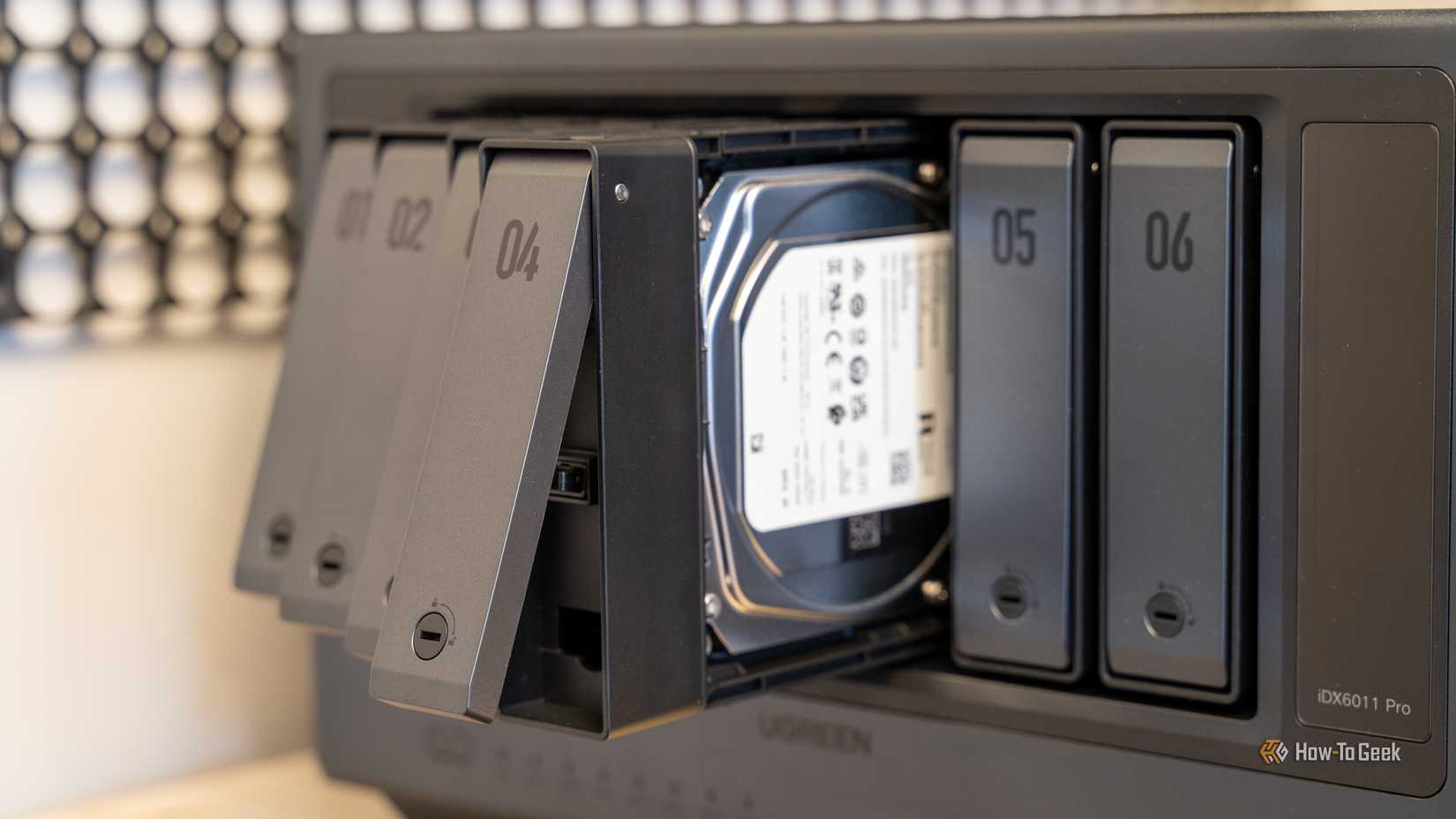 Multiple drive trays pulled out from the Ugreen iDX6011 Pro NAS with a hard drive visible inside the bay.