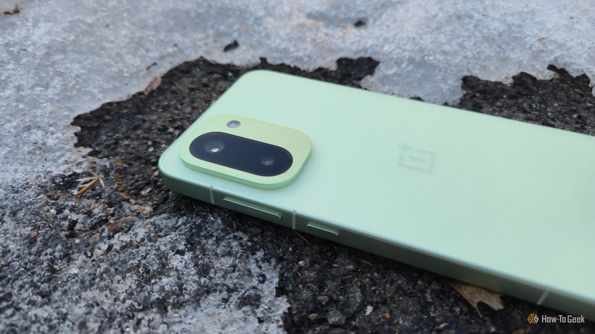 OnePlus 15R facedown on asphalt and surrounded by ice.