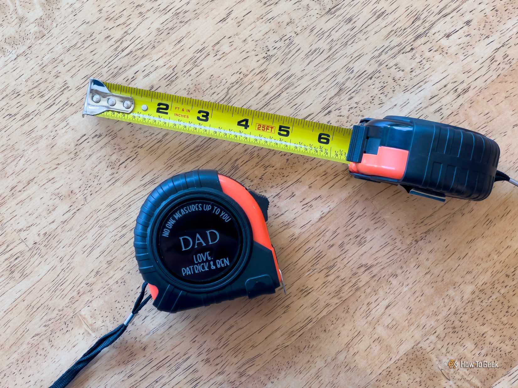 A custom engraved tape measure sits next to a pulled-out measuring tape on a wooden table.