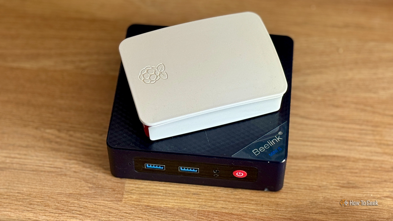 A Raspberry Pi in a case lying on top of a Beelink Mini S12 Pro mini PC.