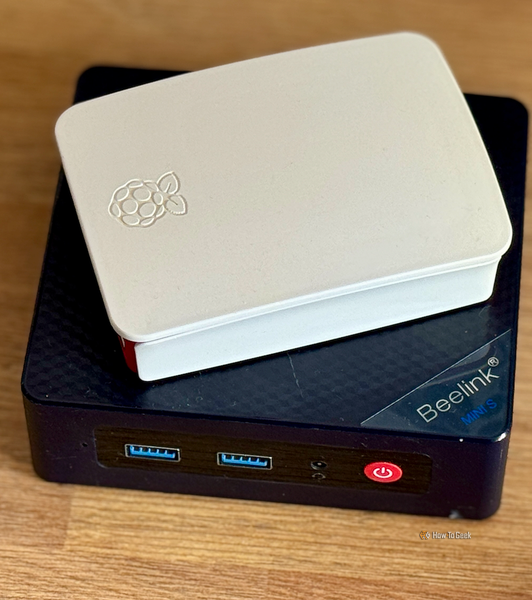 A Raspberry Pi in a case lying on top of a Beelink Mini S12 Pro mini PC.