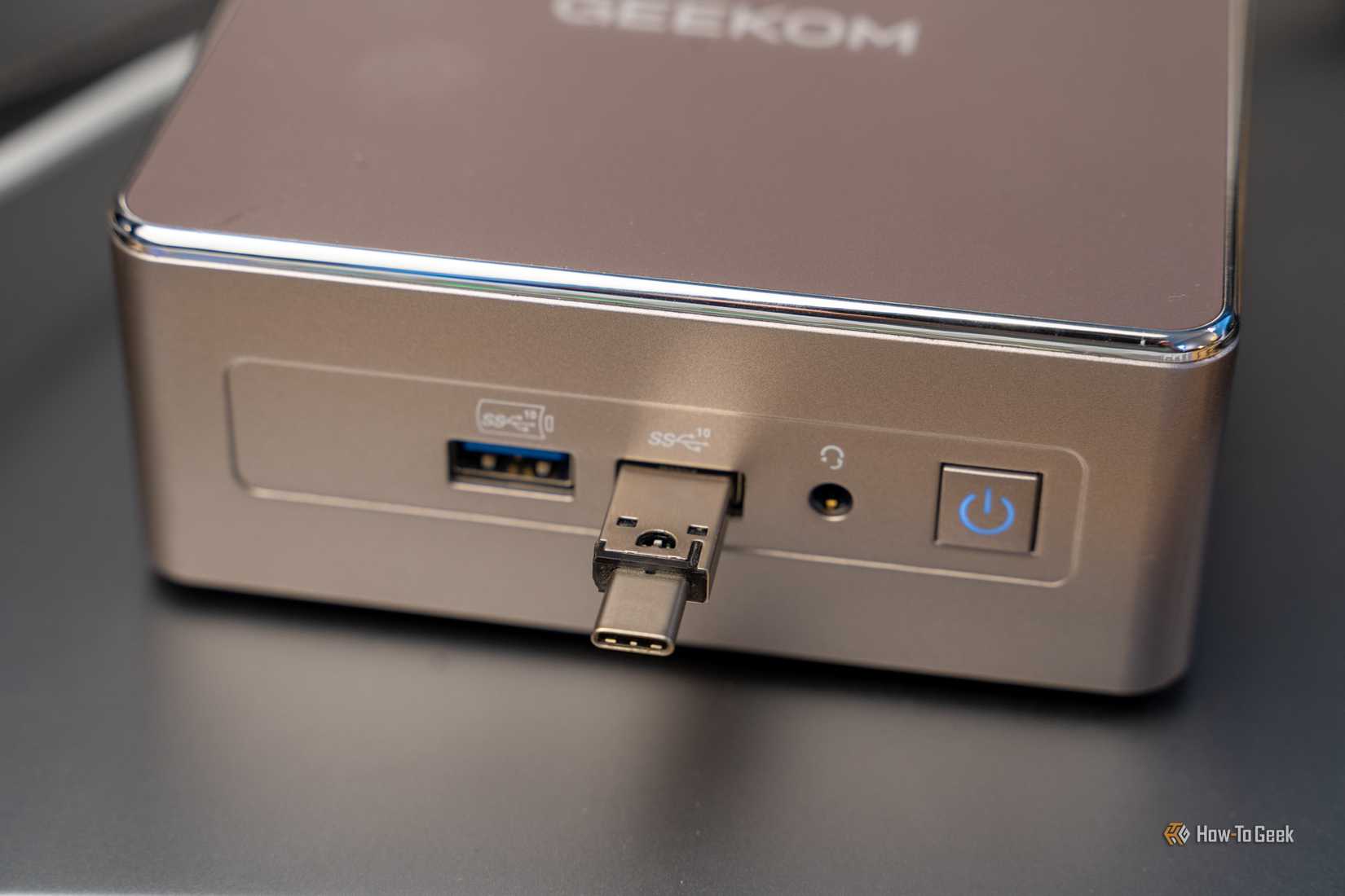 A small Geekom mini PC with a USB-C flash drive plugged into the front panel.