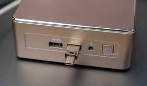 A small Geekom mini PC with a USB-C flash drive plugged into the front panel.
